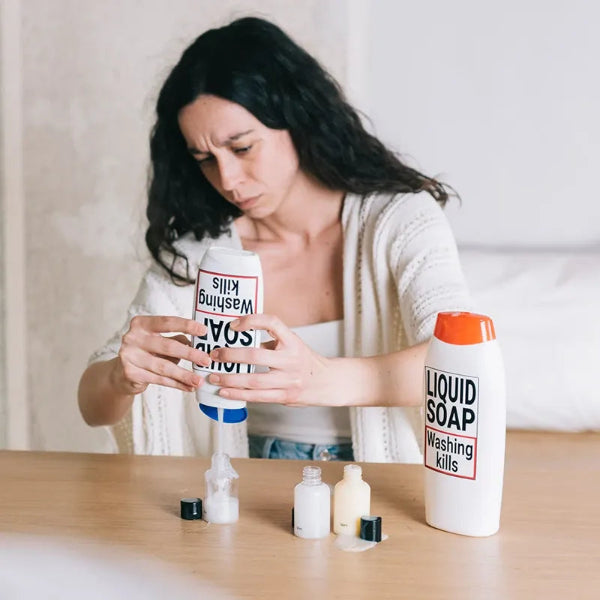 Woman holding a bottle of liquid soap with a visible label on a wooden surface.