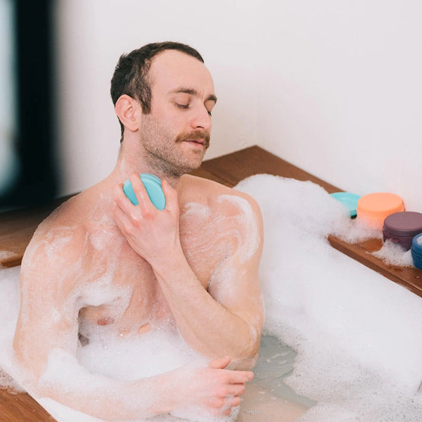 Man in a bathtub with bubbles and bath bombs, enjoying a relaxing moment.
